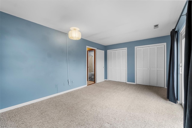 unfurnished bedroom with baseboards, carpet floors, visible vents, and multiple closets