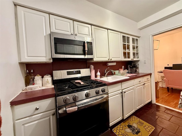 kitchen featuring glass insert cabinets, white cabinetry, stainless steel appliances, and a sink