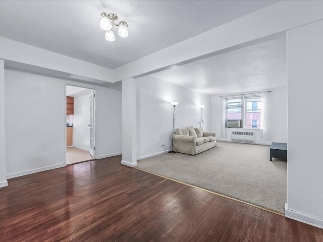 unfurnished living room featuring cooling unit, wood finished floors, baseboards, radiator, and carpet