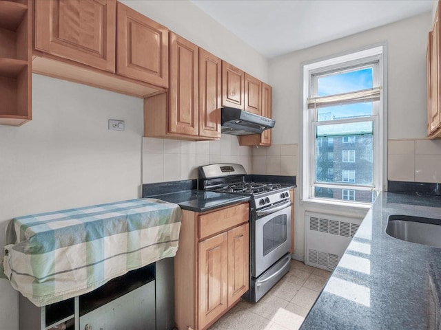 kitchen featuring tasteful backsplash, radiator, gas stove, dark stone counters, and under cabinet range hood