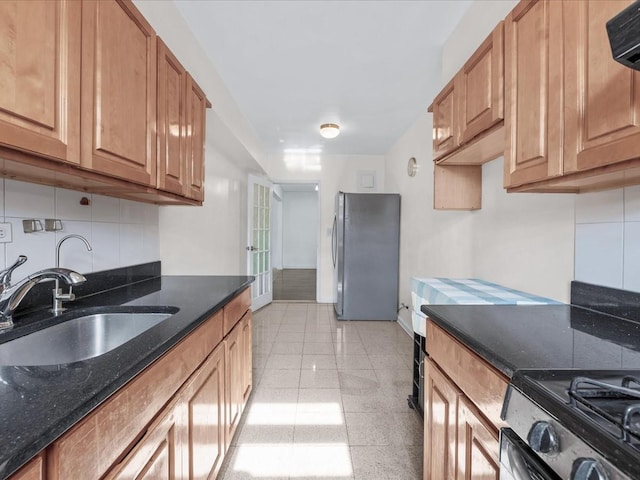 kitchen featuring baseboards, decorative backsplash, dark stone countertops, stainless steel appliances, and a sink