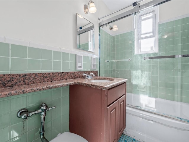 bathroom featuring toilet, bath / shower combo with glass door, vanity, and tile walls