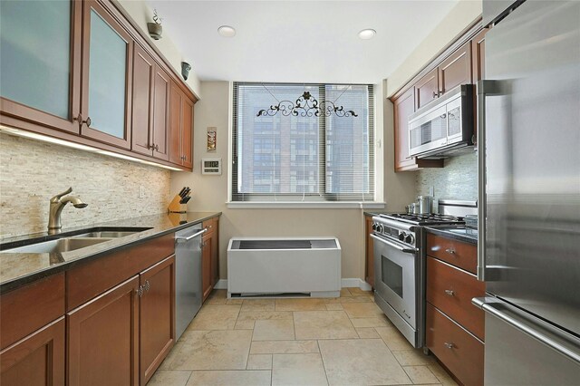 kitchen with baseboards, appliances with stainless steel finishes, dark stone countertops, a sink, and backsplash