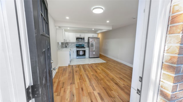 kitchen featuring decorative backsplash, appliances with stainless steel finishes, light countertops, light wood-type flooring, and white cabinetry