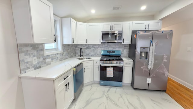 kitchen featuring tasteful backsplash, light stone counters, stainless steel appliances, white cabinetry, and a sink