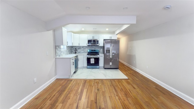 kitchen featuring stainless steel appliances, white cabinetry, vaulted ceiling, light countertops, and tasteful backsplash