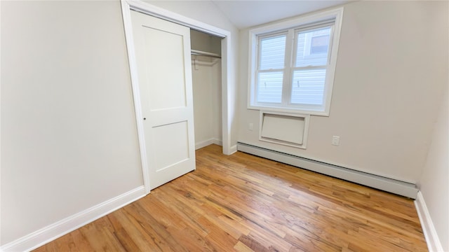 unfurnished bedroom featuring a baseboard radiator, baseboards, light wood-style flooring, and a closet