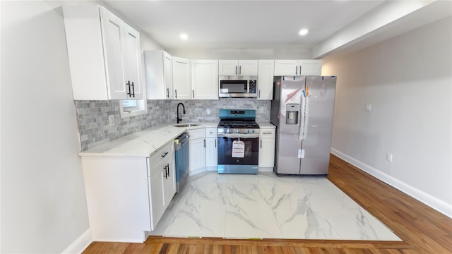 kitchen with stainless steel appliances, white cabinetry, a sink, and backsplash