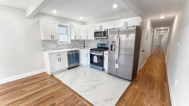 kitchen with baseboards, white cabinets, marble finish floor, appliances with stainless steel finishes, and backsplash