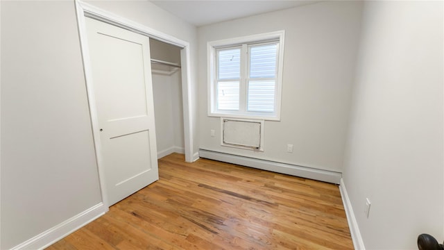 unfurnished bedroom with light wood-style floors, a baseboard radiator, baseboards, and a closet