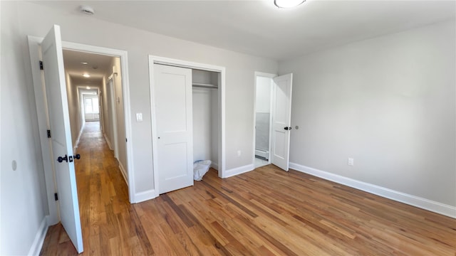 unfurnished bedroom featuring baseboard heating, a closet, light wood-type flooring, and baseboards