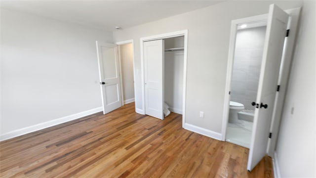 unfurnished bedroom with a closet, baseboards, connected bathroom, and light wood finished floors