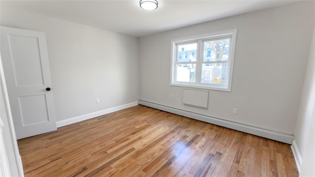 spare room with a baseboard heating unit, baseboards, and light wood finished floors