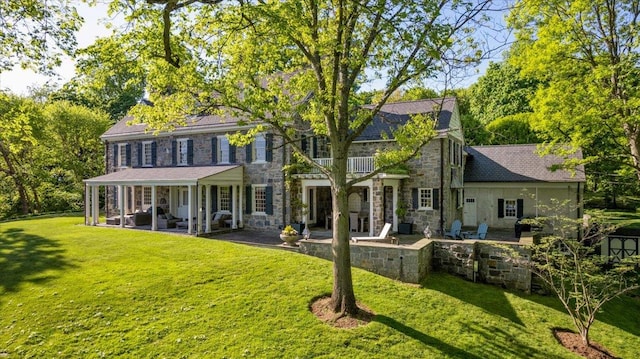 colonial-style house with stone siding, a patio area, and a front lawn