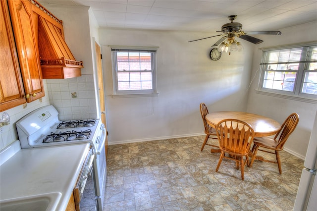 dining room featuring stone finish flooring, a healthy amount of sunlight, ceiling fan, and baseboards