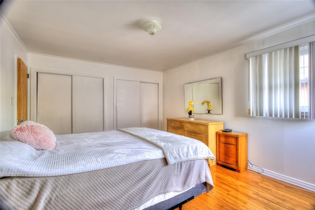 bedroom featuring baseboards, light wood finished floors, and multiple closets