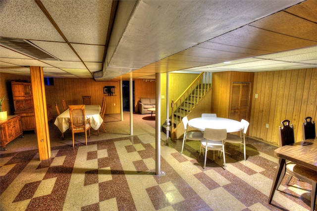 finished basement with wood walls, stairway, a drop ceiling, and tile patterned floors