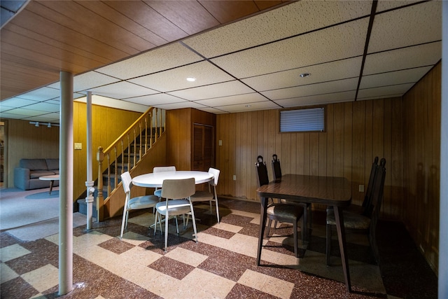 dining space featuring stairs, wooden walls, a paneled ceiling, and tile patterned floors