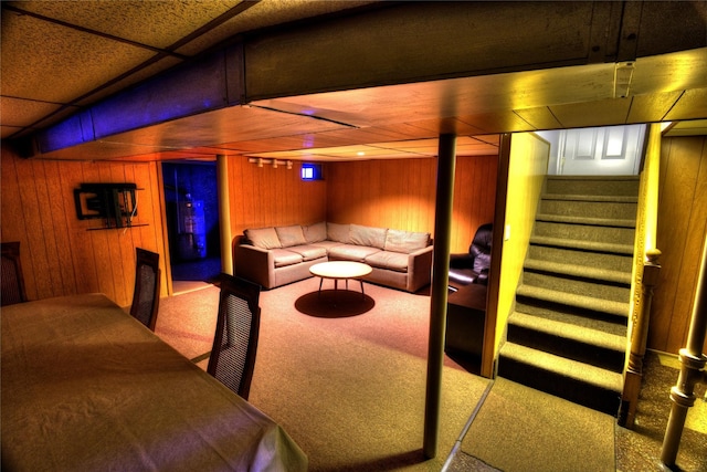 living room with carpet floors, a paneled ceiling, wooden walls, and stairs