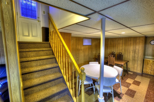 interior space featuring stairs, a drop ceiling, wooden walls, and tile patterned floors