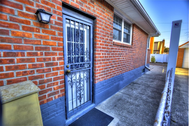 view of exterior entry featuring brick siding and fence