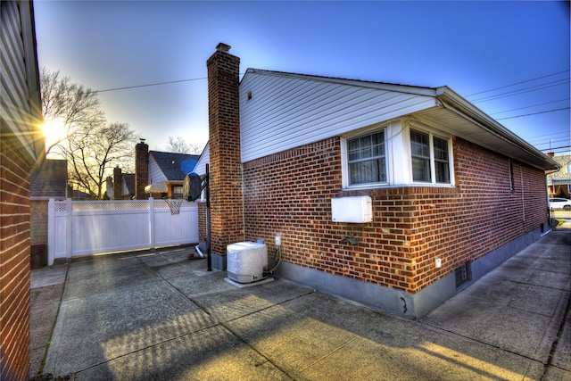 property exterior at dusk with a patio area, fence, and brick siding