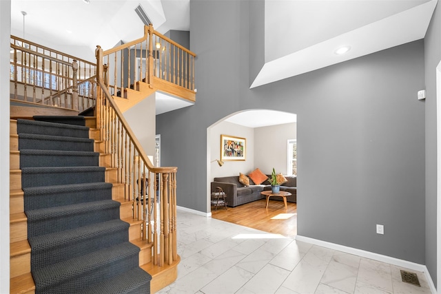 staircase with baseboards, visible vents, arched walkways, marble finish floor, and a high ceiling