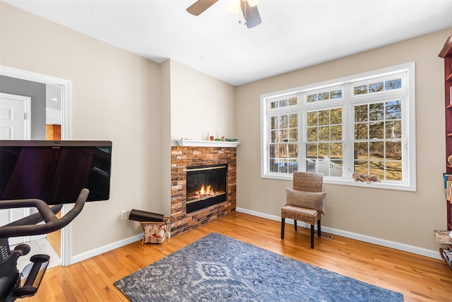 sitting room with a ceiling fan, a brick fireplace, baseboards, and wood finished floors