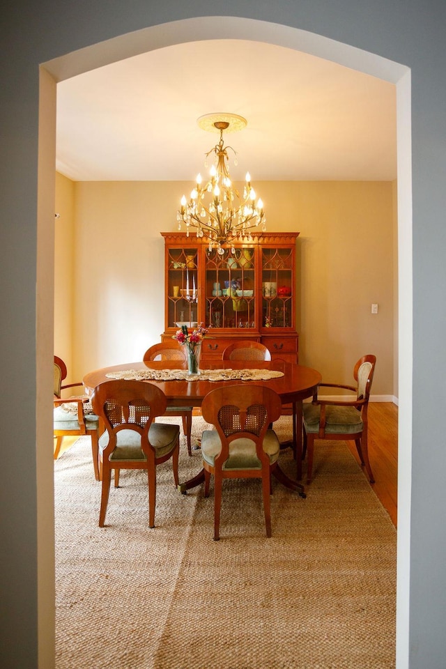 dining room with arched walkways, baseboards, wood finished floors, and a notable chandelier