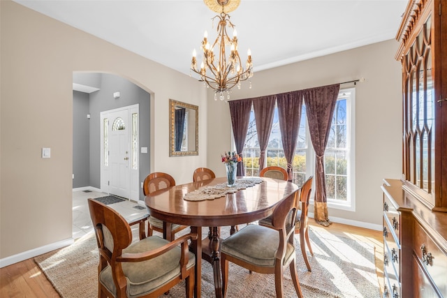 dining area with arched walkways, a notable chandelier, light wood-style flooring, and baseboards