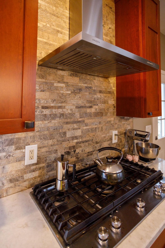 kitchen featuring wall chimney exhaust hood, brown cabinets, light countertops, and stainless steel gas stovetop