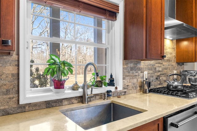 kitchen with tasteful backsplash, wall chimney exhaust hood, light stone counters, appliances with stainless steel finishes, and a sink