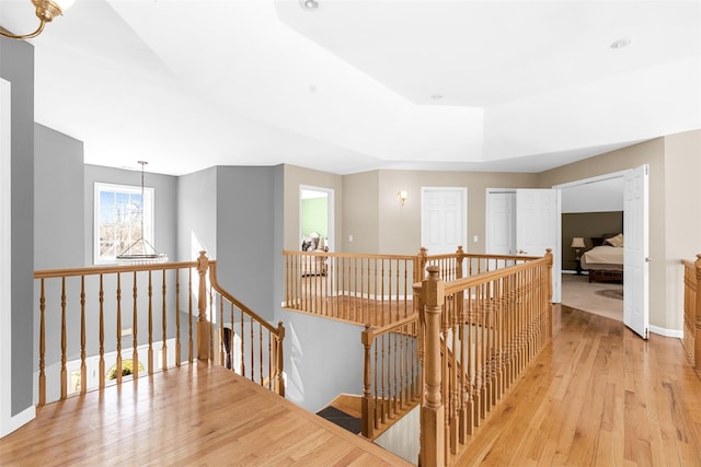 corridor with light wood-type flooring, baseboards, a chandelier, and an upstairs landing