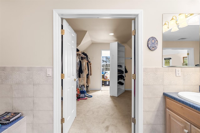 bathroom featuring a wainscoted wall, vanity, tile walls, vaulted ceiling, and a spacious closet