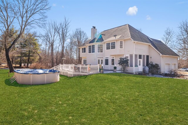 rear view of house with a covered pool, a chimney, roof with shingles, a deck, and a yard