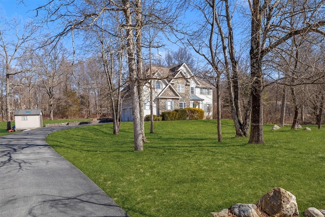 shingle-style home with a storage shed, stone siding, aphalt driveway, an outbuilding, and a front yard