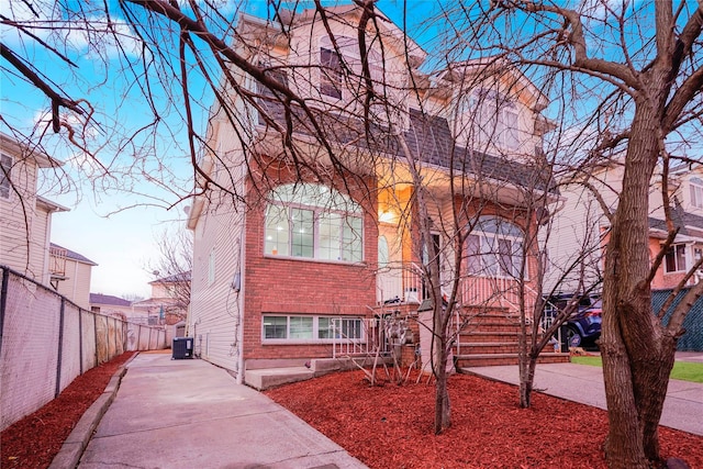 view of front of property featuring driveway, fence, cooling unit, and brick siding