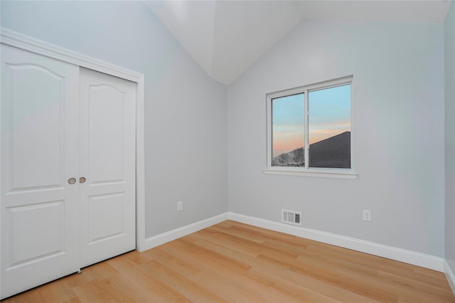 unfurnished bedroom featuring lofted ceiling, visible vents, baseboards, a closet, and light wood-type flooring