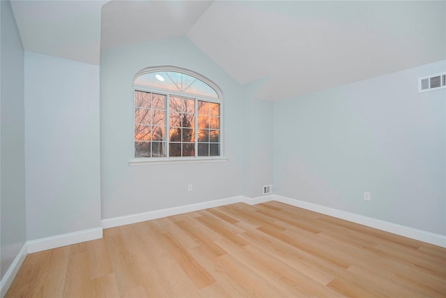 spare room featuring light wood-style floors, lofted ceiling, visible vents, and baseboards