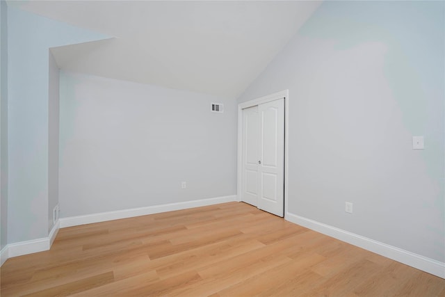 spare room with lofted ceiling, light wood finished floors, visible vents, and baseboards