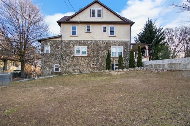 back of house with stone siding, fence, and stucco siding