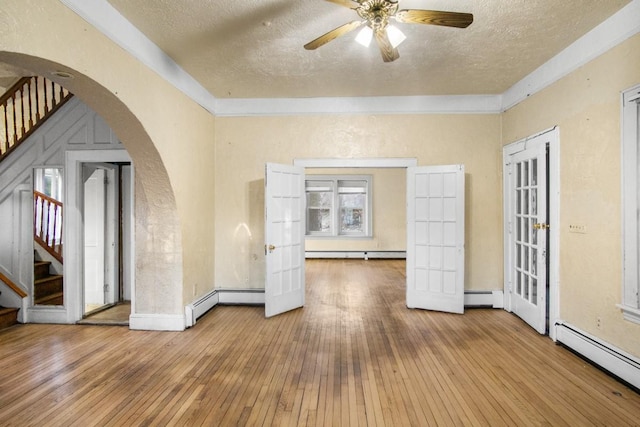 spare room featuring stairs, arched walkways, a baseboard heating unit, and a baseboard radiator