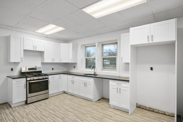 kitchen featuring white cabinets, dark countertops, stainless steel range with gas stovetop, light wood-type flooring, and a sink