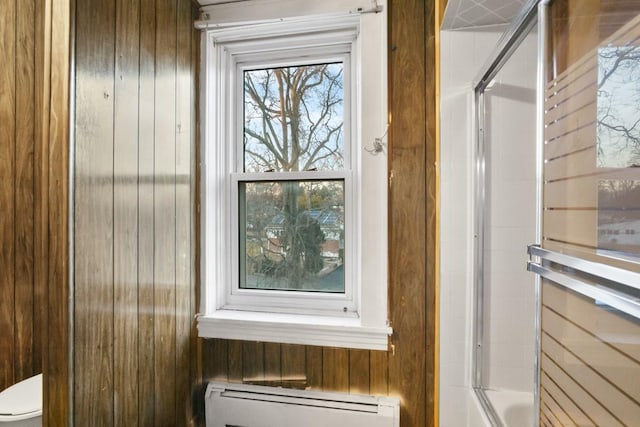 details featuring toilet, wooden walls, baseboard heating, and an enclosed shower