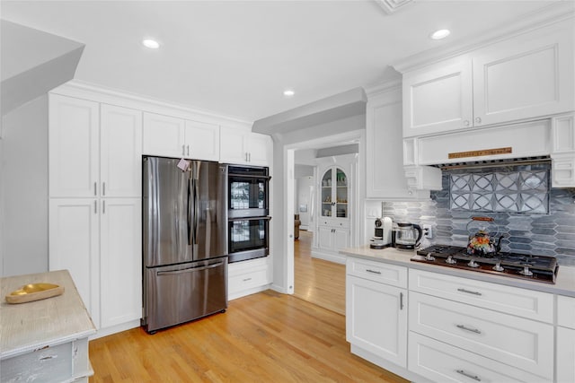 kitchen with appliances with stainless steel finishes, backsplash, light wood-style flooring, and white cabinets