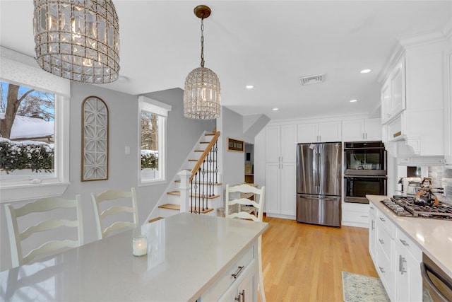 kitchen with a healthy amount of sunlight, light wood finished floors, appliances with stainless steel finishes, and a notable chandelier