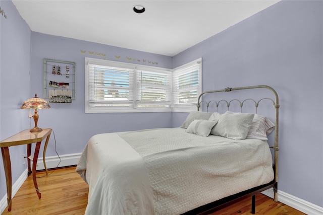 bedroom featuring a baseboard heating unit, baseboards, and wood finished floors