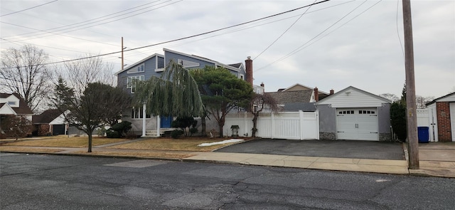 view of property hidden behind natural elements with a garage, fence, aphalt driveway, and an outdoor structure