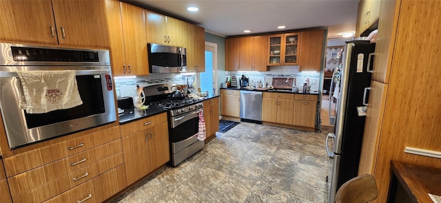 kitchen with dark countertops, backsplash, stainless steel appliances, and a sink