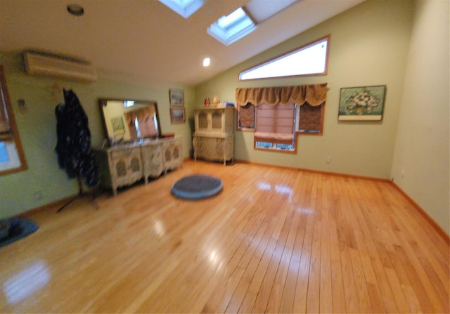 interior space featuring vaulted ceiling with skylight, a wall unit AC, baseboards, and hardwood / wood-style flooring